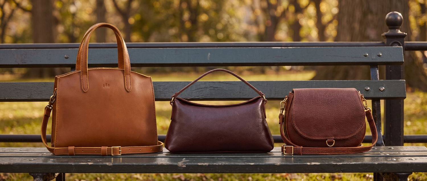 Two models outdoors by a lake wearing matching pink and red striped apparel, each carrying a brown crossbody bag. Featured bags are Metro Crossbody Bag in Honey and Circle Crossbody Bag in Coldbrew.