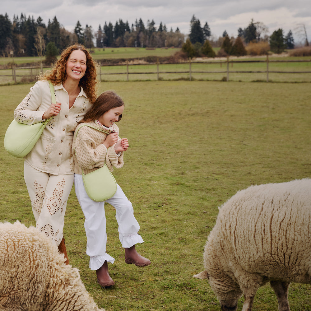 Woman and child walking through a field with sheep wearing a Olivia Shoulder bag and a Petal Crossbody bag in Shadow Lime