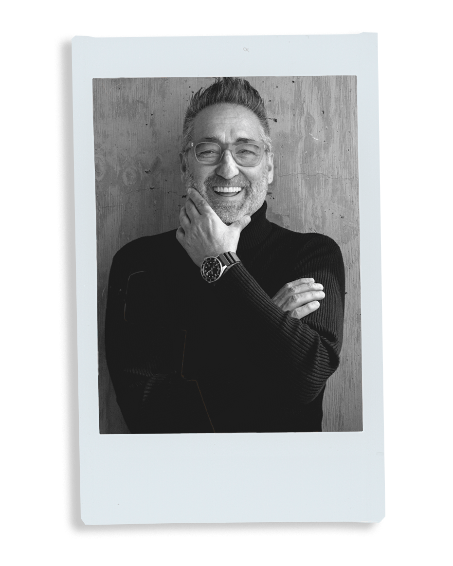 Black and white photo of a smiling man with glasses and a watch, framed as a Polaroid.