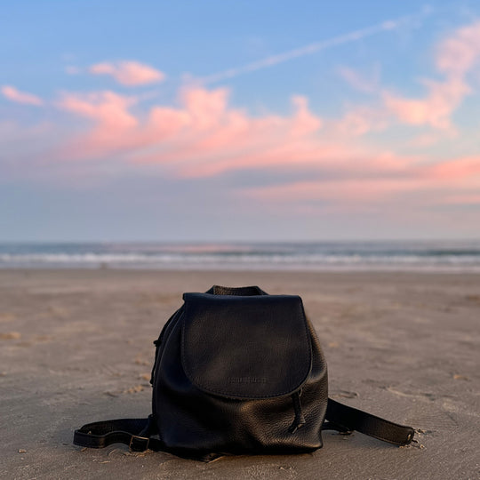 A Bucket Backpack in Coldbrew on a sandy beach with a colorful sky