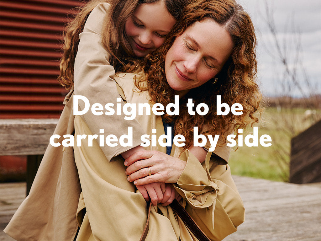 A child hugging a woman outdoors with text 'Designed to be carried side by side'.