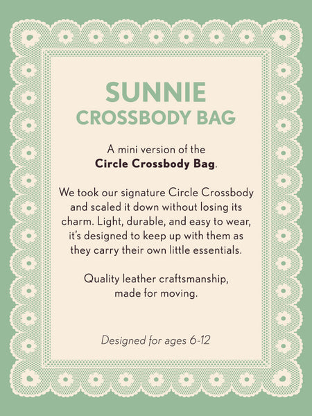 Product description card for a Sunnie crossbody bag on a green background with decorative border. Text says: Sunny Crossbody Bag a mini version of the Circle Crossbody bag. We took our signature Circle Crossbody and scaled it down without losing its charm. Light, durable, and easy to wear, it's designed to keep up with them as they carry their own little essentials. Quality leather craftsmanship, made for moving. Designed for ages 6-12