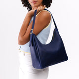 Cobalt Medium | Model holding u-shaped, flat-bottomed leather shoulder bag with adjustable strap