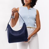 Cobalt Medium | Model holding u-shaped, flat-bottomed leather shoulder bag with adjustable strap