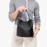 Black Large | Model holding symmetrical bucket bag with handle, latch closure, and removable crossbody strap
