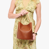 Honey Large | Model holding symmetrical bucket bag with handle, latch closure, and removable crossbody strap