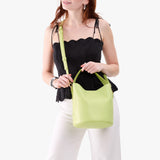 Shadow Lime Large | Model holding symmetrical bucket bag with handle, latch closure, and removable crossbody strap