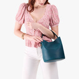 Westward Blue Large | Model carrying symmetrical bucket bag with handle, latch closure, and removable crossbody strap