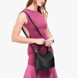 Black Small | Model holding symmetrical bucket bag with handle, latch closure, and removable crossbody strap