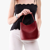 Chili Red Small | Model holding symmetrical bucket bag with handle, latch closure, and removable crossbody strap