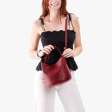 Chili Red Small | Model holding symmetrical bucket bag with handle, latch closure, and removable crossbody strap