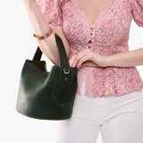 Evergreen Small | Model holding symmetrical bucket bag with handle, latch closure, and removable crossbody strap