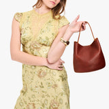 Nutmeg Small | Model holding symmetrical bucket bag with handle, latch closure, and removable crossbody strap
