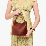 Nutmeg Small | Model holding symmetrical bucket bag with handle, latch closure, and removable crossbody strap