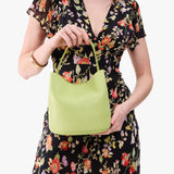 Shadow Lime Small | Model holding symmetrical bucket bag with handle, latch closure, and removable crossbody strap