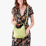 Shadow Lime Small | Model holding symmetrical bucket bag with handle, latch closure, and removable crossbody strap