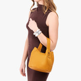 Sunshine Small | Model carrying symmetrical bucket bag with handle, latch closure, and removable crossbody strap