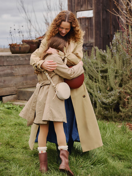 A woman and child hugging while wearing a circle crossbody in Nutmeg and a Sunnie Crossbody in Pebbled Bone