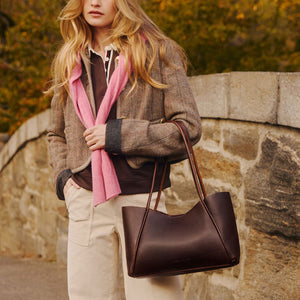 A model outdoors carrying a large dark leather tote bag. 
