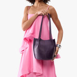 Empire Small | Model wearing sleeveless pink dress holding petite bucket shaped tote bag with matching leather handles