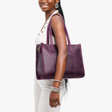 Larkspur East/West | Model holding structured wide tote bag with overlapping panels and crossbody strap