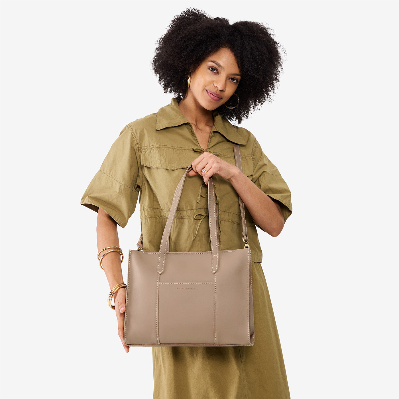Stone*East/West | Model holding structured wide tote bag with overlapping panels and crossbody strap