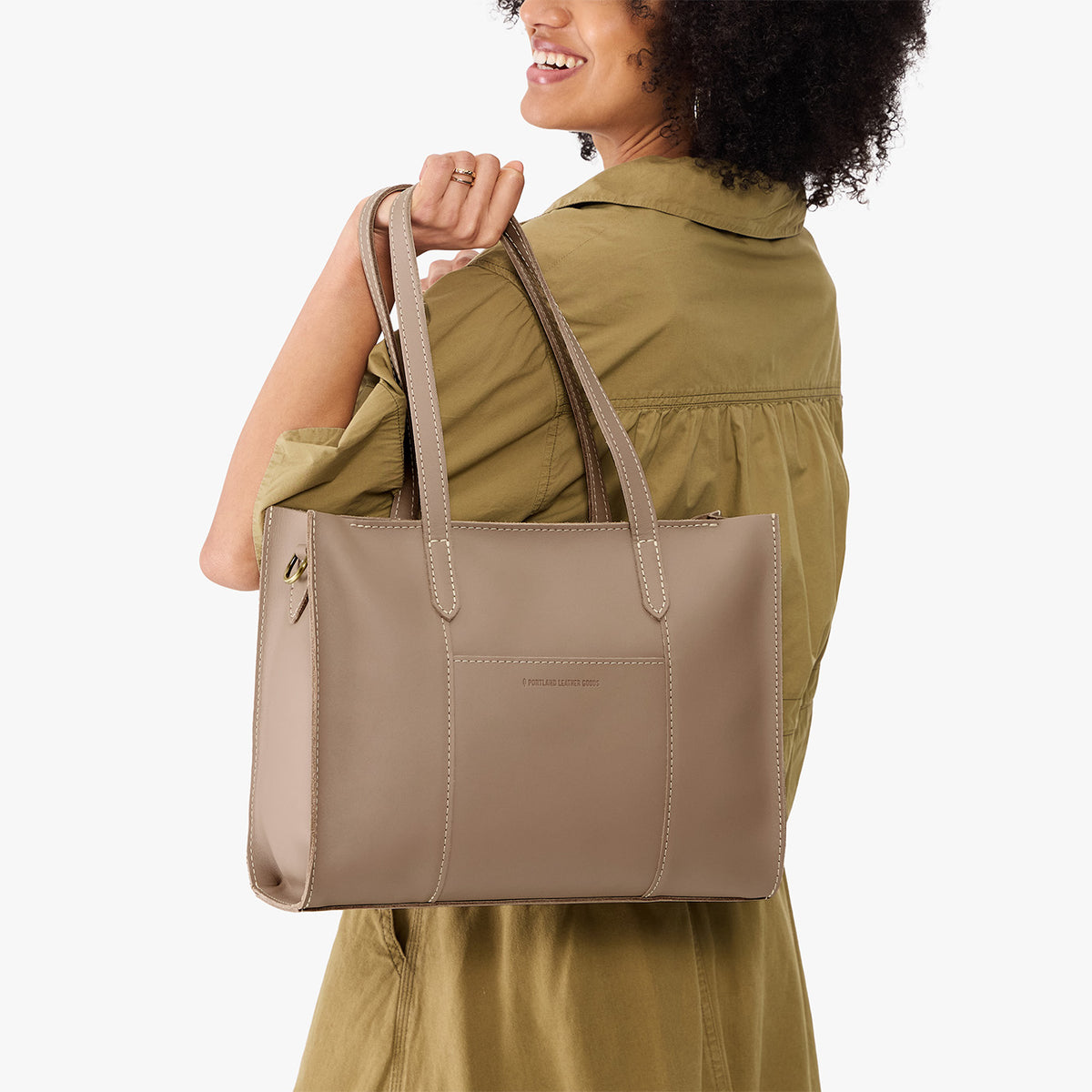Stone*East/West | Model holding structured wide tote bag with overlapping panels and crossbody strap