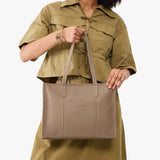 Stone East/West | Model holding structured wide tote bag with overlapping panels and crossbody strap