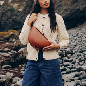 A model wearing a Koala Sling in the color Honey with a rainy beach background