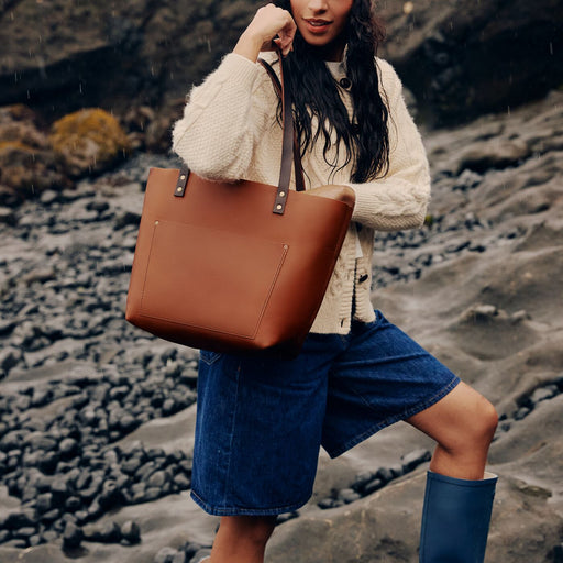A model walking up a stoney hill carrying a Honey Classic Leather Tote in the rain. featured image