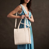 Pebbled Bone North/South | Model holding structured large tote bag with overlapping panels and crossbody 