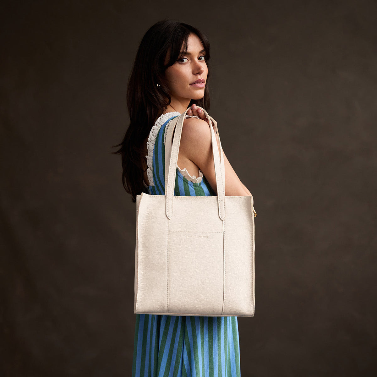Pebbled Bone*North/South | Model holding structured large tote bag with overlapping panels and crossbody 