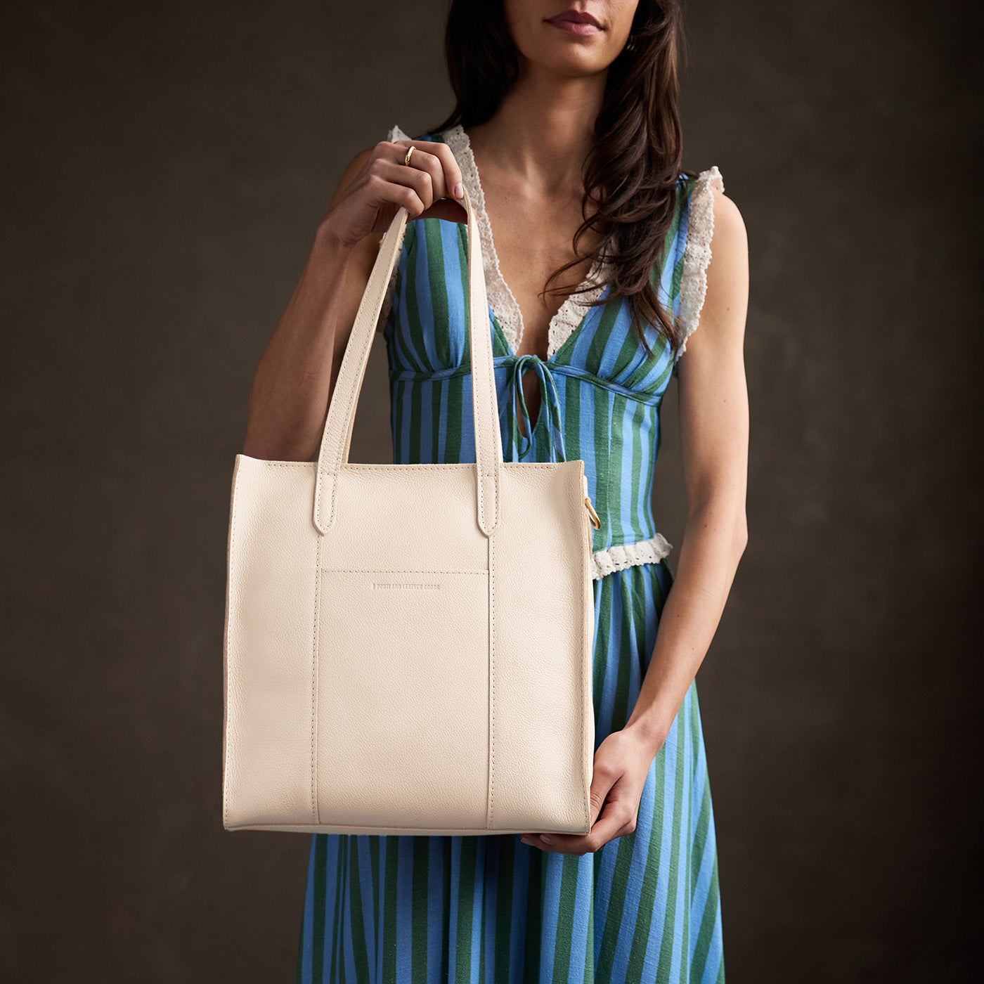 Pebbled Bone*North/South | Model holding structured large tote bag with overlapping panels and crossbody 