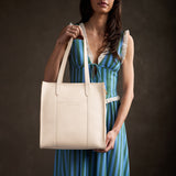 Pebbled Bone North/South | Model holding structured large tote bag with overlapping panels and crossbody 
