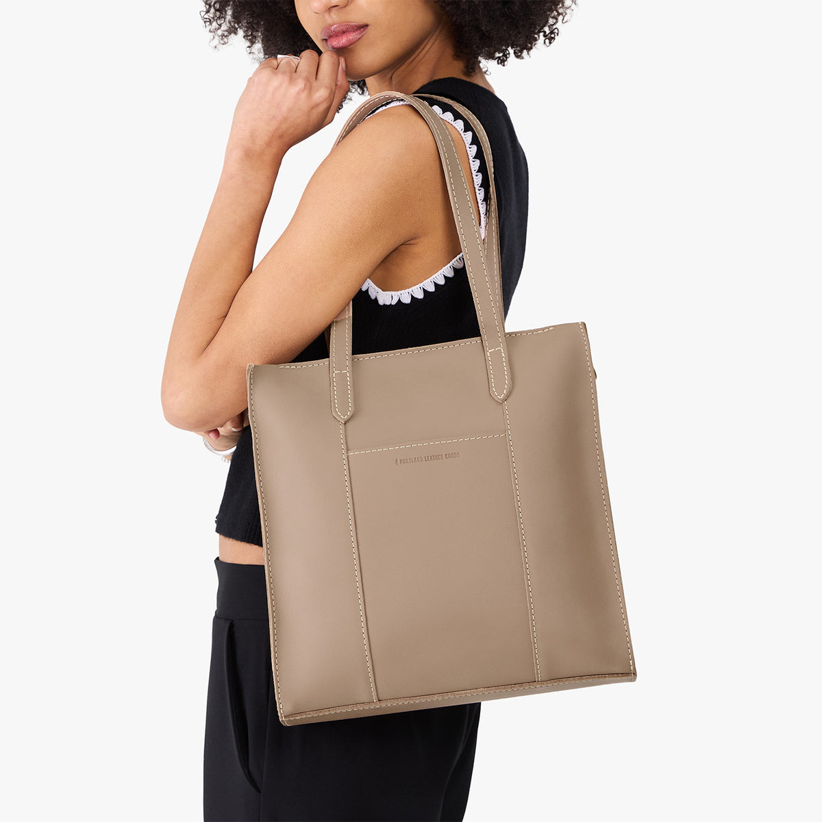 Stone*North/South | Model holding structured wide tote bag with overlapping panels and crossbody strap