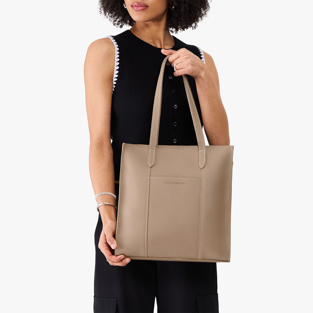 Stone*North/South | Model holding structured wide tote bag with overlapping panels and crossbody strap