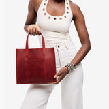 Phoenix | Model holding structured mid-size tote bag with overlapping panels and crossbody strap