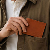 Toscano | A close-up of a person holding a brown leather card holder in their hand and placing it into the chest pocket. The card holder has 'PORTLAND LEATHER' debossed on the bottom right corner.