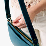 Westward Blue Small | Model holding petite bean shaped shoulder bag with a zipper closure