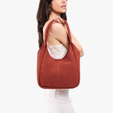 Cinnabar Large | A model holding a u-shaped, flat-bottomed leather shoulder bag with two outside pockets