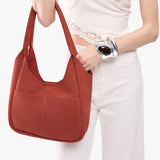Cinnabar Large | A model holding a u-shaped, flat-bottomed leather shoulder bag with two outside pockets