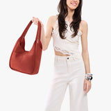 Cinnabar Large | A model holding a u-shaped, flat-bottomed leather shoulder bag with two outside pockets