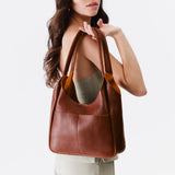 Nutmeg Large | A model holding a u-shaped, flat-bottomed leather shoulder bag with two outside pockets