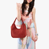 Cinnabar Medium | A model holding a u-shaped, flat-bottomed leather shoulder bag with two outside pockets