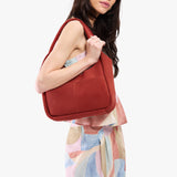 Cinnabar Medium | A model holding a u-shaped, flat-bottomed leather shoulder bag with two outside pockets