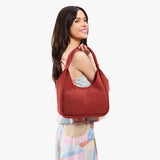 Cinnabar Medium | A model holding a u-shaped, flat-bottomed leather shoulder bag with two outside pockets