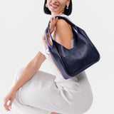 Cobalt Medium | A model holding a u-shaped, flat-bottomed leather shoulder bag with two outside pockets