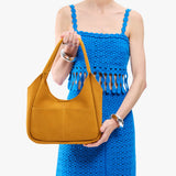 Dijon Medium | A model holding a u-shaped, flat-bottomed leather shoulder bag with two outside pockets