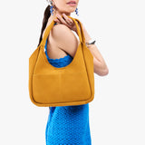 Dijon Medium | A model holding a u-shaped, flat-bottomed leather shoulder bag with two outside pockets