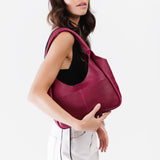 Orchid Medium | A model holding a u-shaped, flat-bottomed leather shoulder bag with two outside pockets